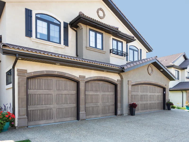 Residential garage doors featuring a modern design, installed on a stylish home with a well-maintained driveway and flower planters, emphasizing quality and curb appeal for homeowners.