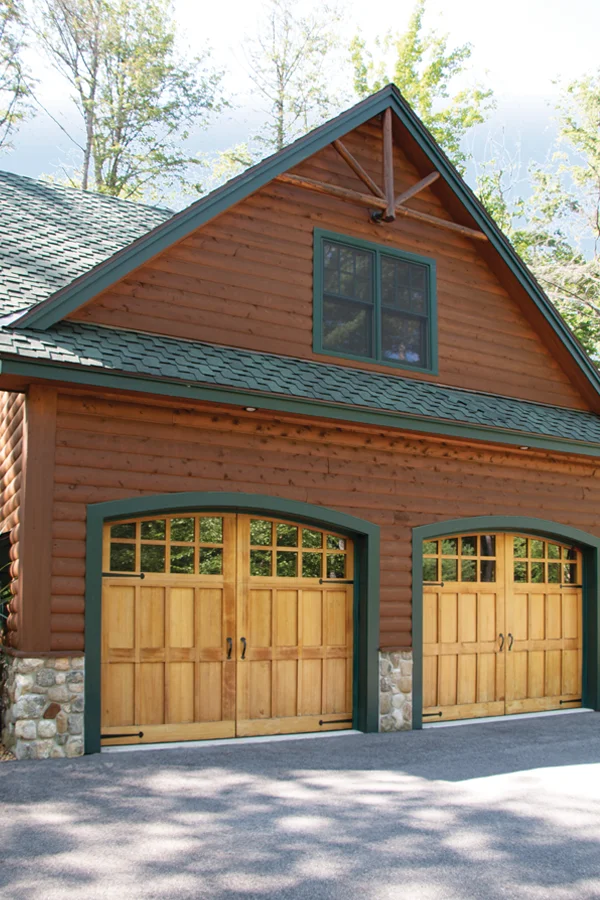 Residential garage with two wooden garage doors featuring arched tops and decorative windows, set against a log cabin exterior, emphasizing durability and aesthetic appeal in Thousand Palms, CA.
