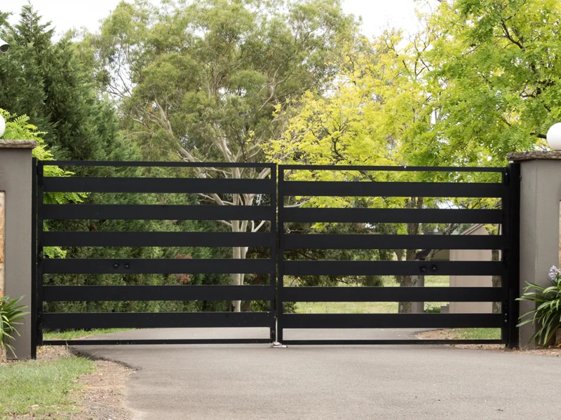 Black sliding gate system with horizontal slats, surrounded by greenery, illustrating secure property access solutions for commercial and industrial facilities.