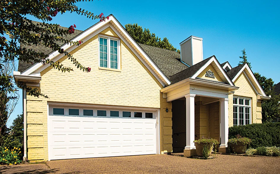Garage with a traditional white finish and decorative windows, enhancing curb appeal of a yellow brick home, emphasizing professional garage door installation in Palm Springs.