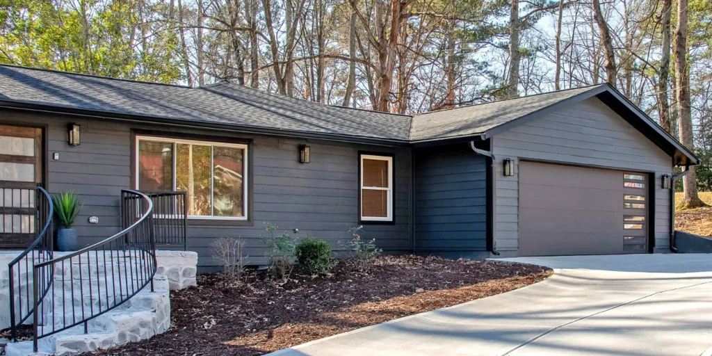 Modern home exterior featuring a dark bronze garage door with double narrow windows, complemented by a stylish stone staircase and landscaped front yard, enhancing overall curb appeal.