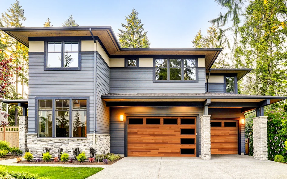 Modern home exterior featuring a two-car garage with wooden doors, landscaped front yard, and large windows, showcasing stylish design and curb appeal relevant to residential garage door services.