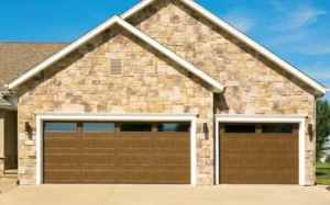 Insulated steel garage doors from the Thermacore® Collection, featuring a rich brown wood grain finish, installed on a home with a stone façade, showcasing design flexibility and thermal efficiency.
