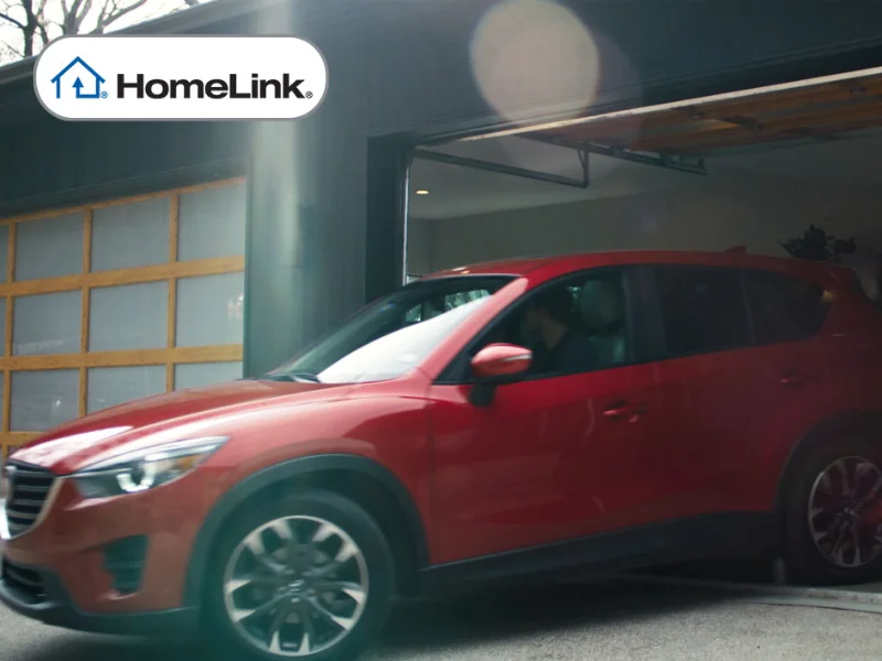 Red SUV exiting garage featuring HomeLink logo, illustrating seamless integration with Overhead Door® garage door opener system for enhanced convenience and security.