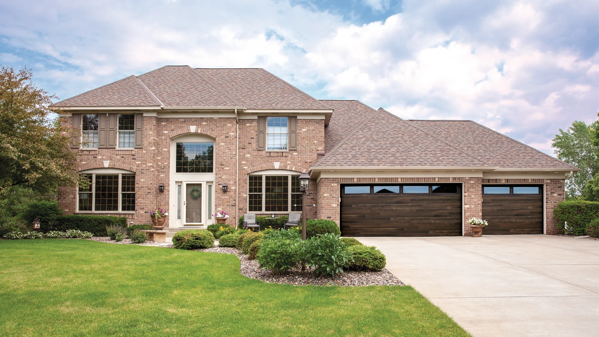 Custom residential garage doors enhancing curb appeal of a brick home with landscaped yard and driveway.