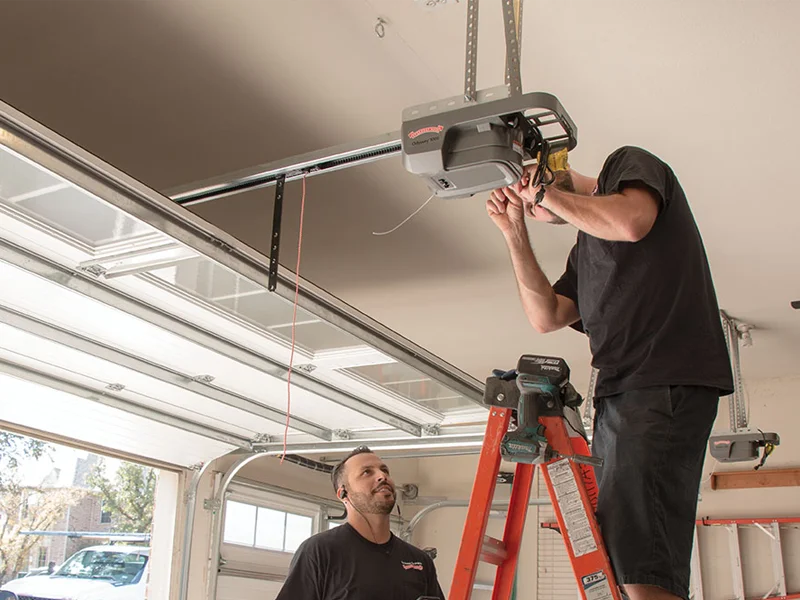Technician repairing garage door opener while another technician observes, demonstrating professional service for garage door maintenance and safety.